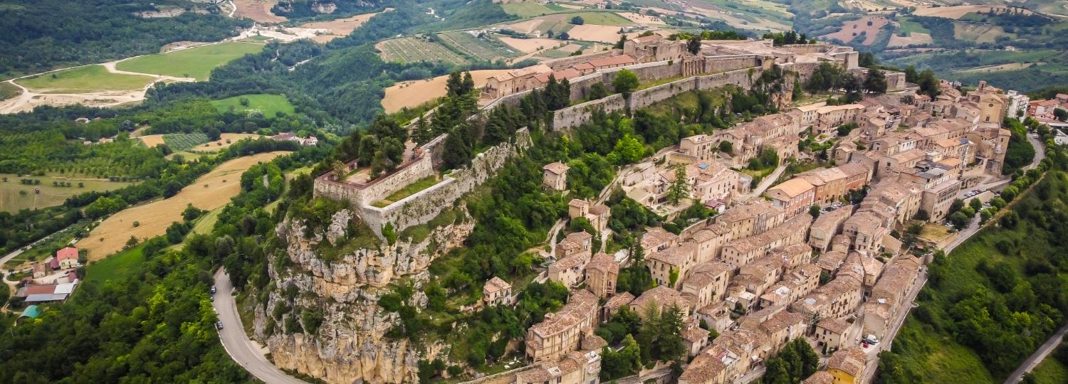 Vista aerea di una città fortificata su una collina, circondata da paesaggi verdi.