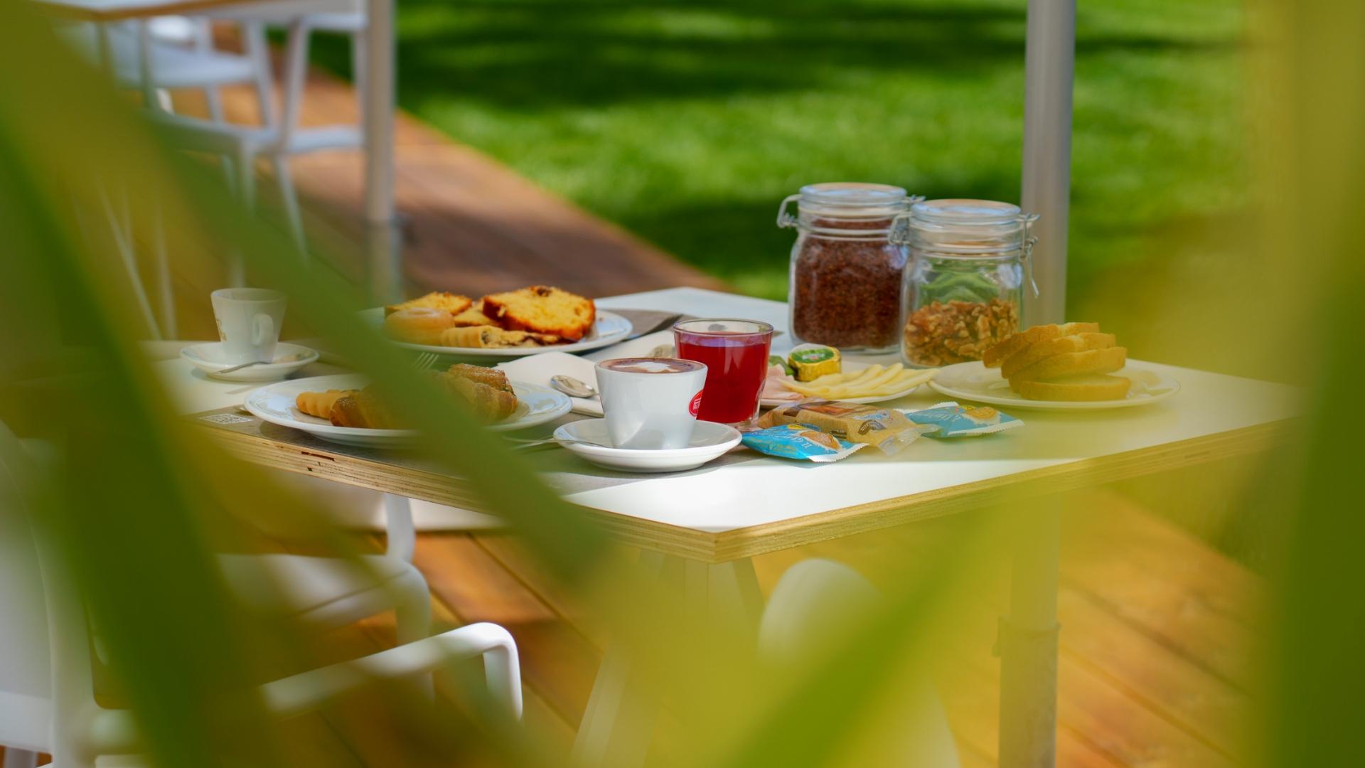 Colazione all'aperto con caffè, succo, dolci e cereali in un giardino soleggiato.