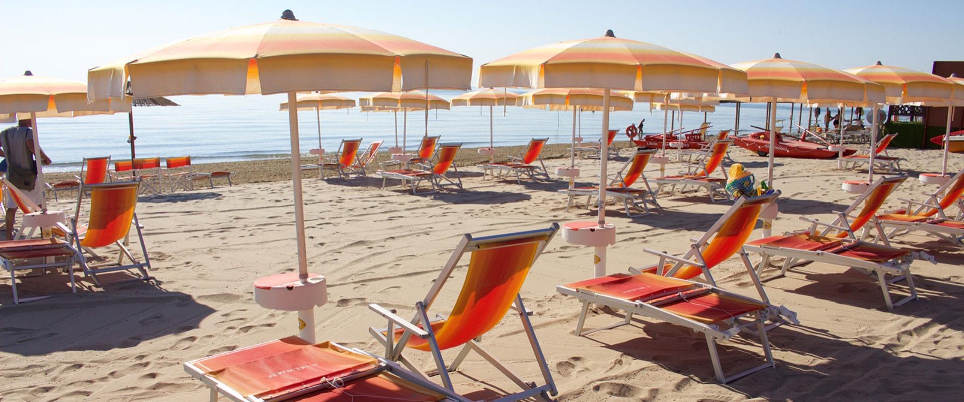 Spiaggia con ombrelloni e lettini arancioni, mare calmo sullo sfondo.