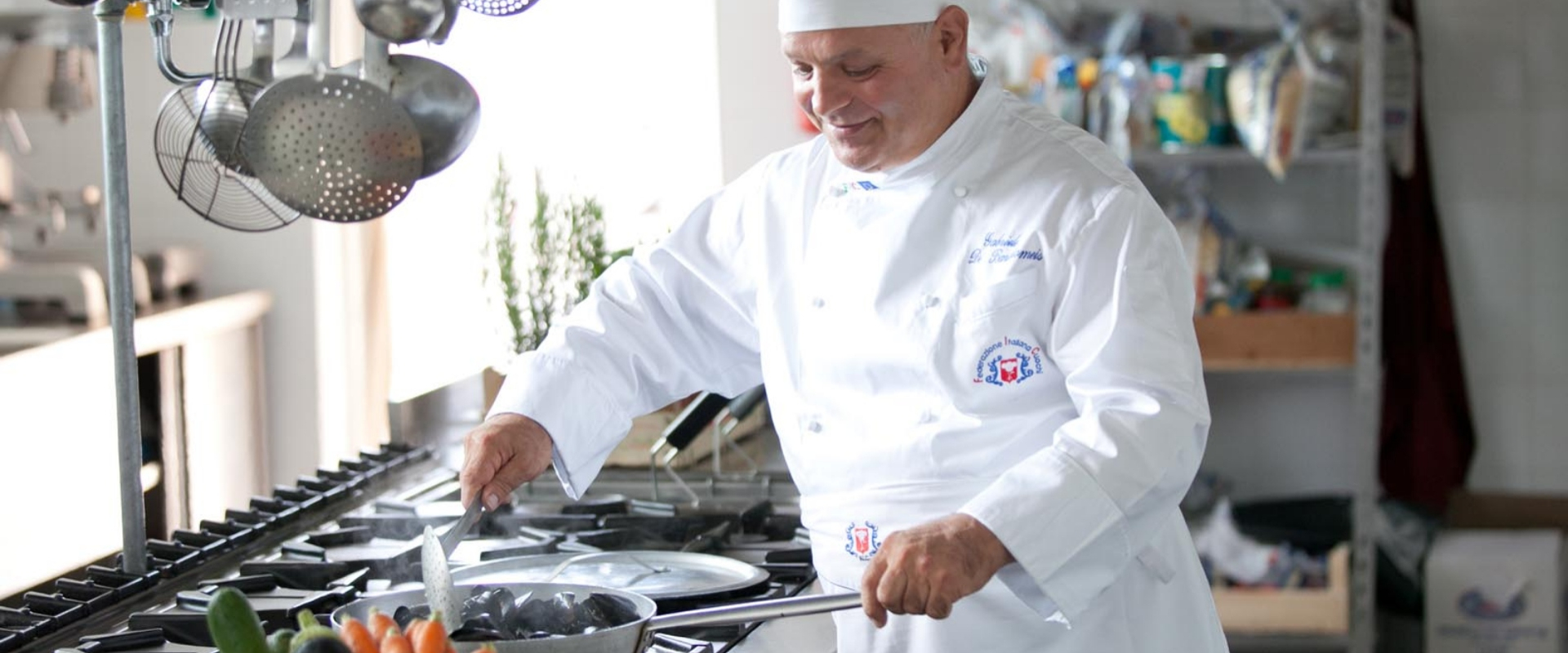 Chef in cucina prepara un piatto con verdure e cozze sul fornello.