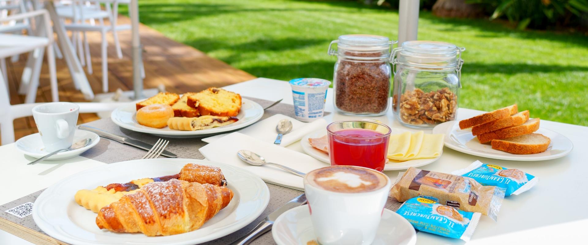 Colazione all'aperto con dolci, caffè e marmellate su tavolo bianco.