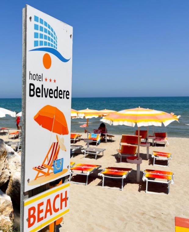 Spiaggia con ombrelloni gialli e arancioni, cartello Hotel Belvedere, mare azzurro.