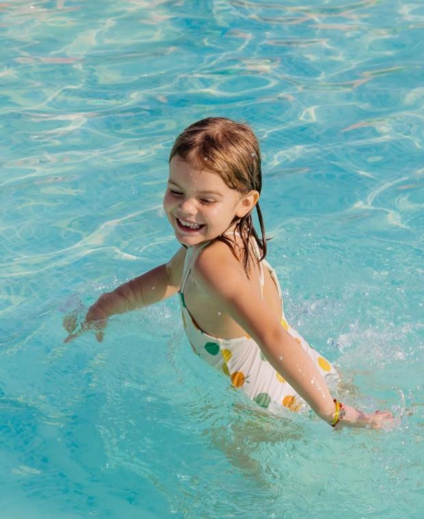 Bambina felice gioca in piscina, indossando un costume a pois colorati.