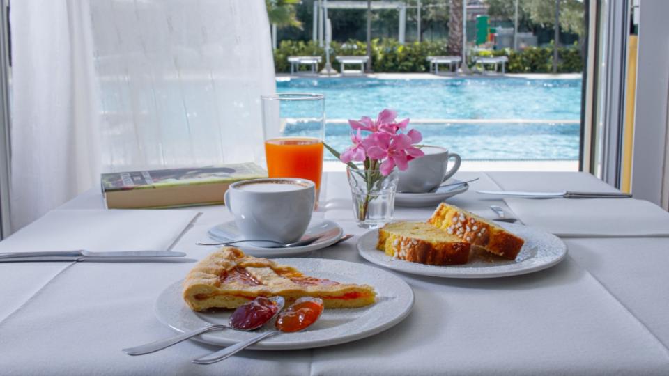 Colazione con dolci e caffè vicino alla piscina, atmosfera rilassante e soleggiata.