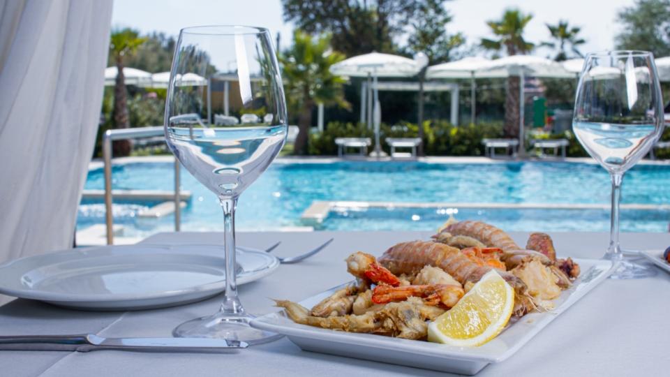 Tavola apparecchiata con piatto di pesce e vista piscina all'aperto.